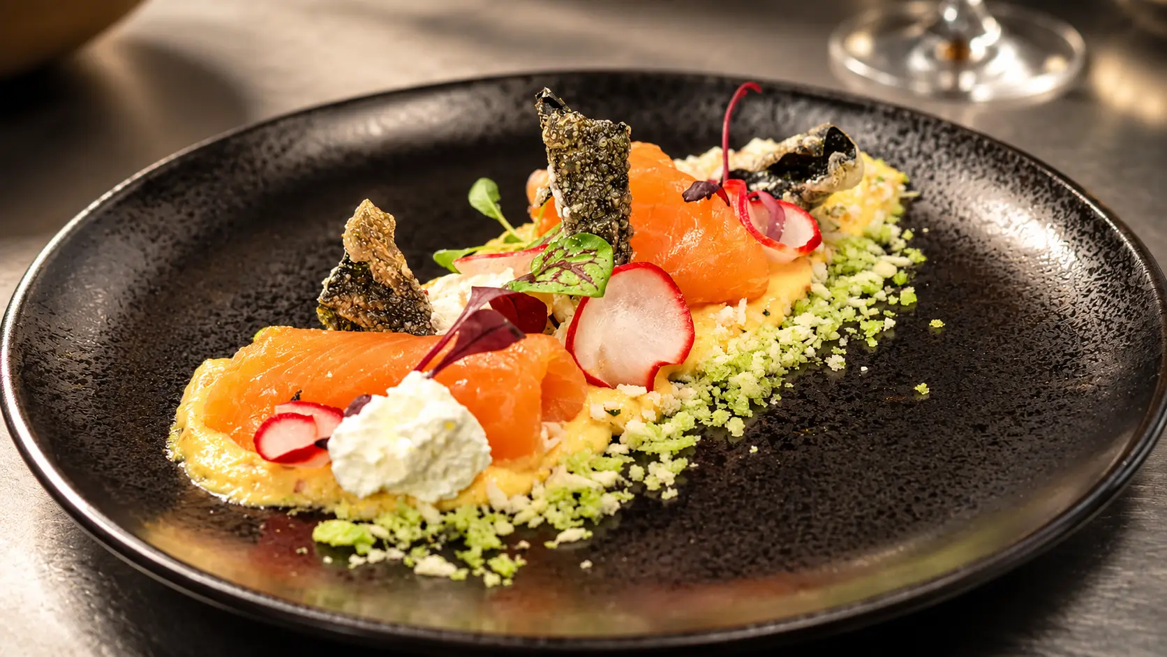 Geräucherter Lachs mit Radieschen, Kräutercrumble und Frischkäse auf schwarzem Teller – Gasthof Kreuz Egerkingen