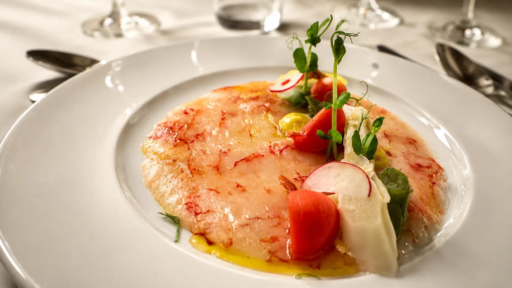 Fisch-Carpaccio mit Radieschen, Fenchel, Tomaten und Kräuteröl auf weissem Teller – Gasthof Kreuz Egerkingen